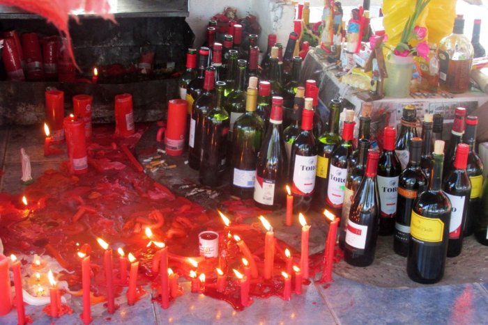 Velas rojas, botellas de vino y cigarrillos encendidos en torno a la figura del santo pagano.